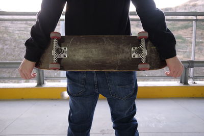 Midsection of man with skateboard standing outdoors