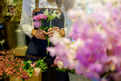 Midsection of florist holding flowers while standing in flower shop