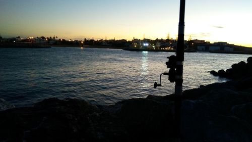 Silhouette people on beach by city against sky during sunset