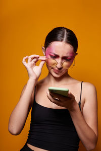 Young woman using mobile phone against yellow wall