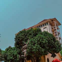 Low angle view of tree by building against clear sky