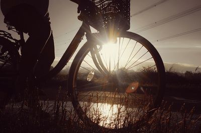 Bicycle by trees against sky during sunset