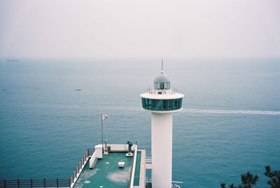 Lighthouse on beach against cloudy sky