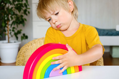 Little boy plays with rainbow colored wooden toys at white table cozy room background. eco lifestyle