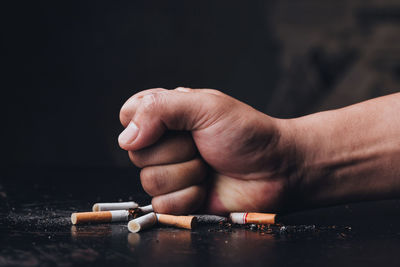 Cropped hand of person crushing cigarette against black background