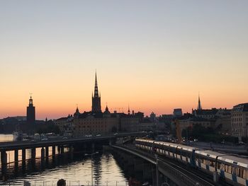 Bridge over river by buildings against sky during sunset