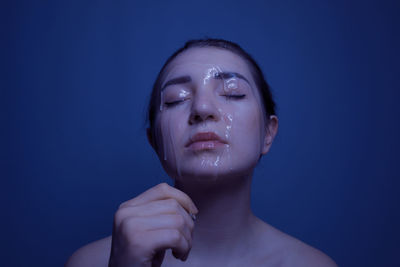 Close-up of shirtless young woman with beauty product on face against blue background