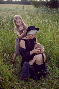 Mother in an evening dress and retro camera with two daughters green field with grass in the summer