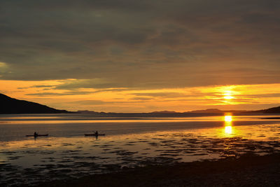 Scenic view of sea against sky during sunset with people kayaking