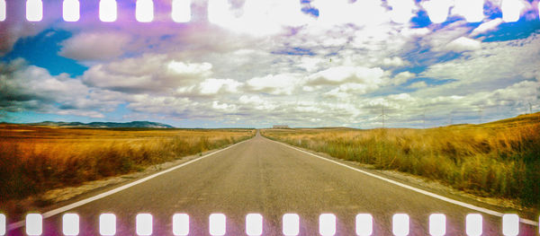 Empty road amidst field against sky