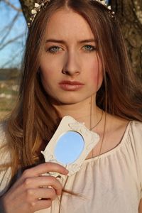 Portrait of beautiful teenage girl holding mirror while standing in forest