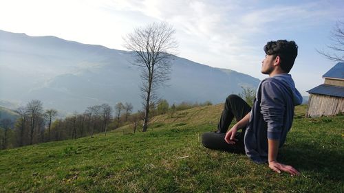 Young man relaxing on grassy field against sky