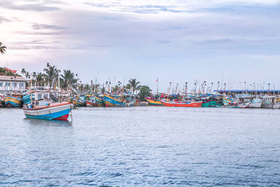 Fishing boats moored at harbor against sky