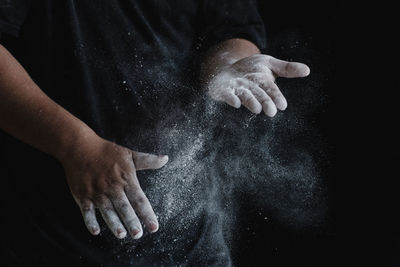 Midsection of person holding cigarette against black background