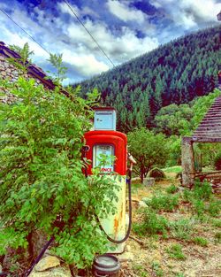 Red telephone booth by trees against sky