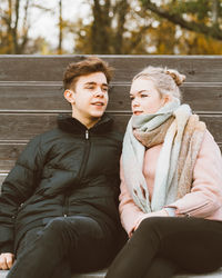 Young couple sitting on bench at park during autumn