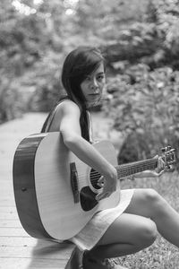 Portrait of woman playing guitar while sitting on boardwalk