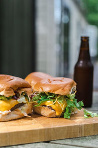 A set of cheeseburgers on a wooden plate and a couple of beers on an outdoor table. suburban.