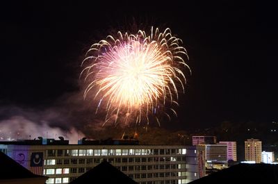 Firework display in city against sky at night
