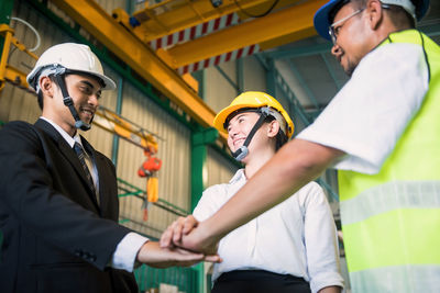 Low angle view of smiling engineers stacking hands in factory