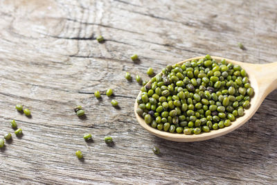 High angle view of scattered mung beans with spoon on wooden table
