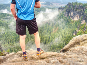 Hiker climbing on sunrise mountain peak rock. slim legs of hiker with hiking boots on exposed rock