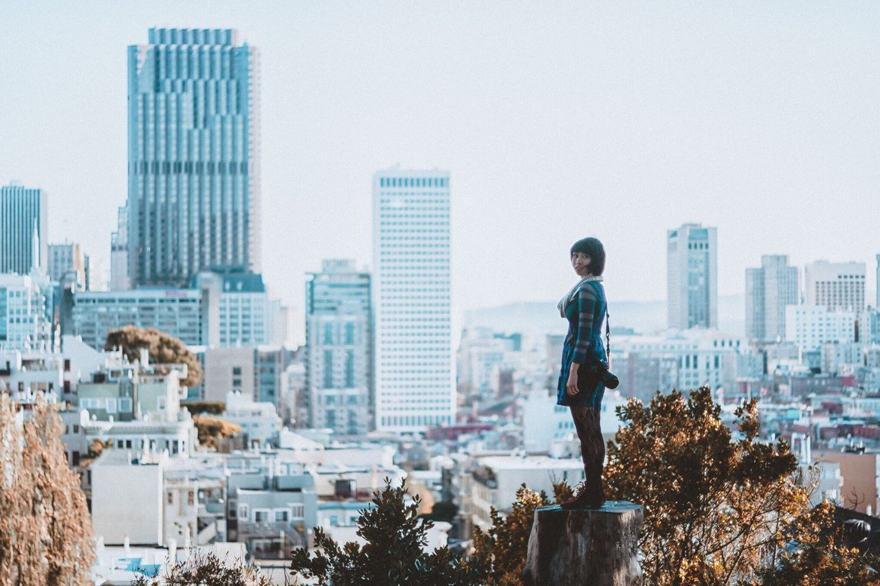 building exterior, city, architecture, built structure, cityscape, lifestyles, clear sky, leisure activity, casual clothing, city life, skyscraper, young adult, standing, modern, copy space, tall - high, residential structure, sky