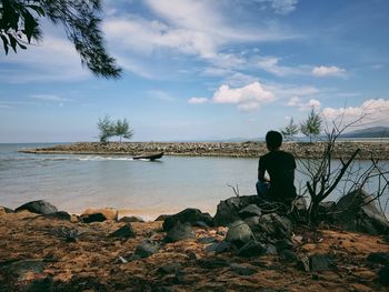 Rear view of man sitting at beach against sky