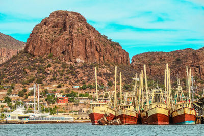 Sailboats moored on sea by mountains against sky