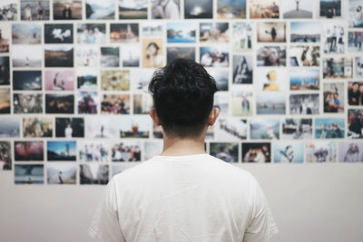 Rear view of man standing against photographs on wall