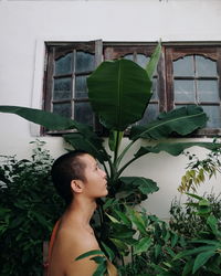 Side view of monk standing amidst plants by house