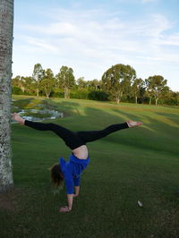 Side view of woman doing handstand on field against sky