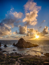 Sugarloaf rock in sea against cloudy sky during sunset