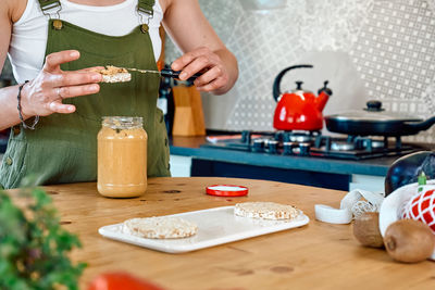 Woman making healthy breakfast or brunch, spreading peanut butter on a puffed corn cakes.