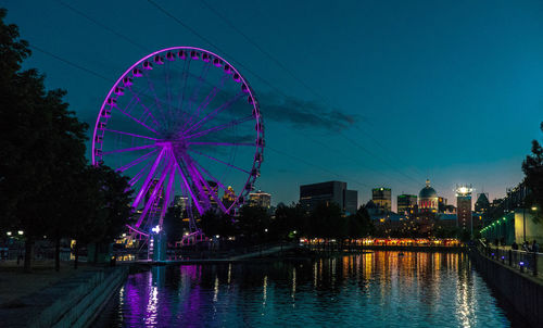 Illuminated ferris wheel in city against sky at night