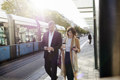 Colleagues waiting at tram stop and using phones