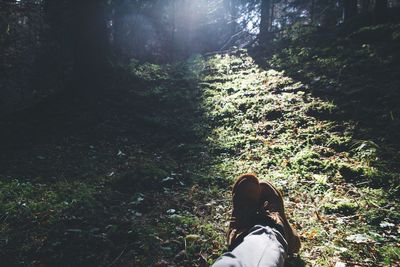 Low section of man with legs crossed at ankle resting on grassy field in forest