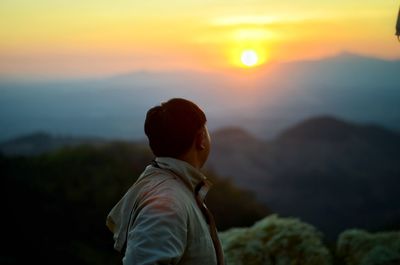 Rear view of man looking at mountain during sunset