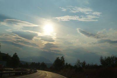 Road by trees against sky during sunset