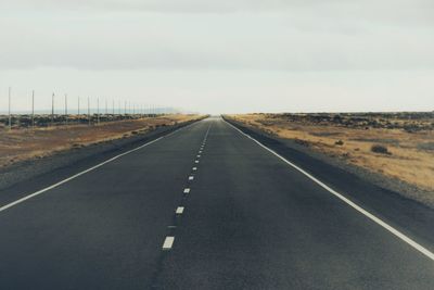 Empty road along landscape against cloudy sky