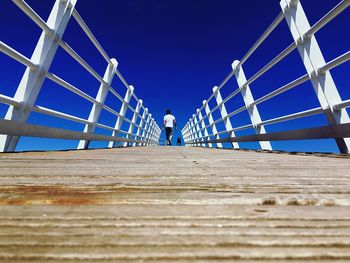 Low angle view of woman on footbridge against clear blue sky