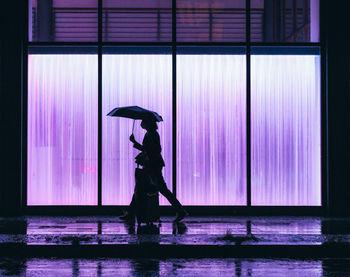 Side view of silhouette woman standing against illuminated wall at night