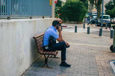 Side view of man sitting on bench in footpath