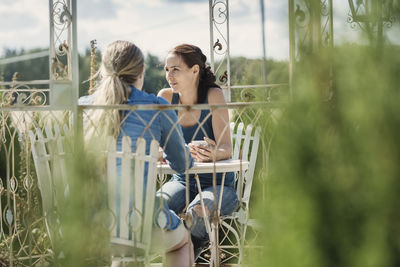 Mid adult female friends with coffee sitting in back yard