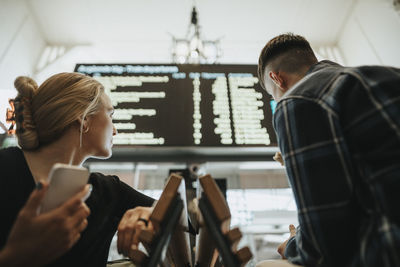 Woman holding smart phone while looking at arrival departure board