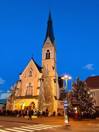 Illuminated christmas tree by building against blue sky