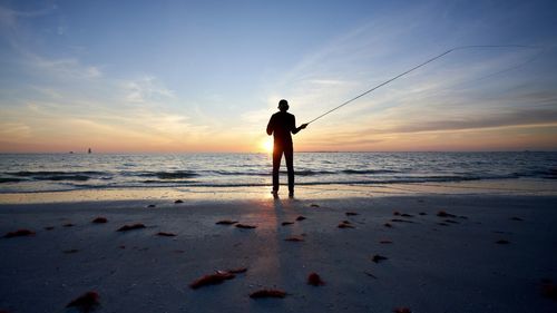 Rear view of man standing on beach during sunset