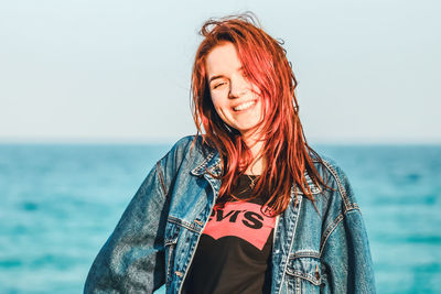 Portrait of smiling young woman standing against sea