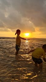 Full length of boys on beach against sky during sunset