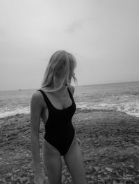 Young woman standing at beach against sky